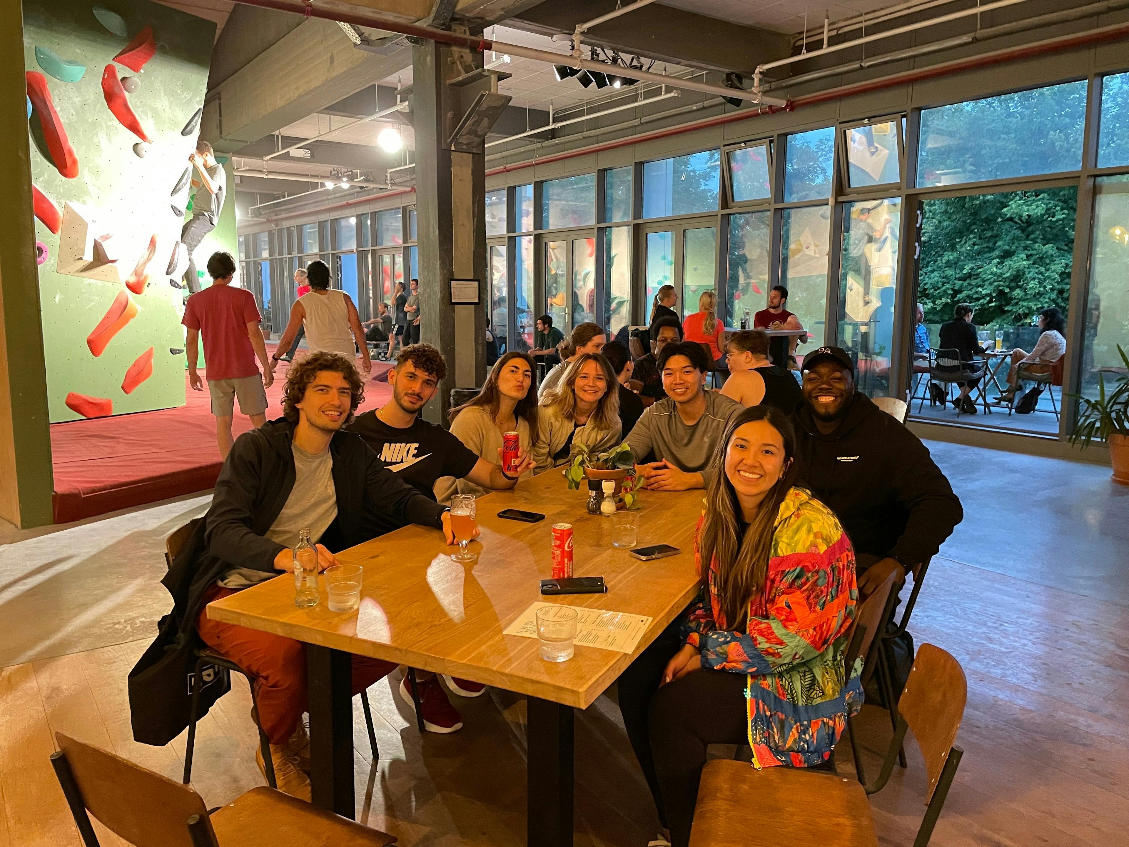 A group of coworkers gathering around a table. In the background are people rock climbing.